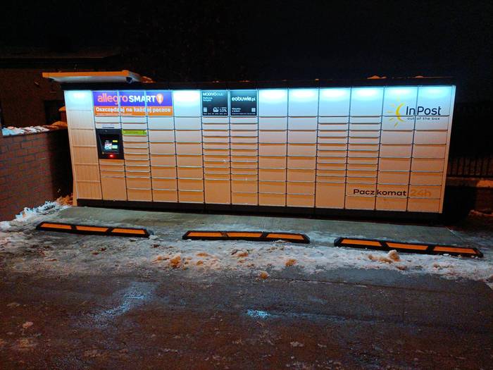 Paczkomat DGO58M równolegle do płotu na parkingu po lewej stronie od bramy wjazdowej