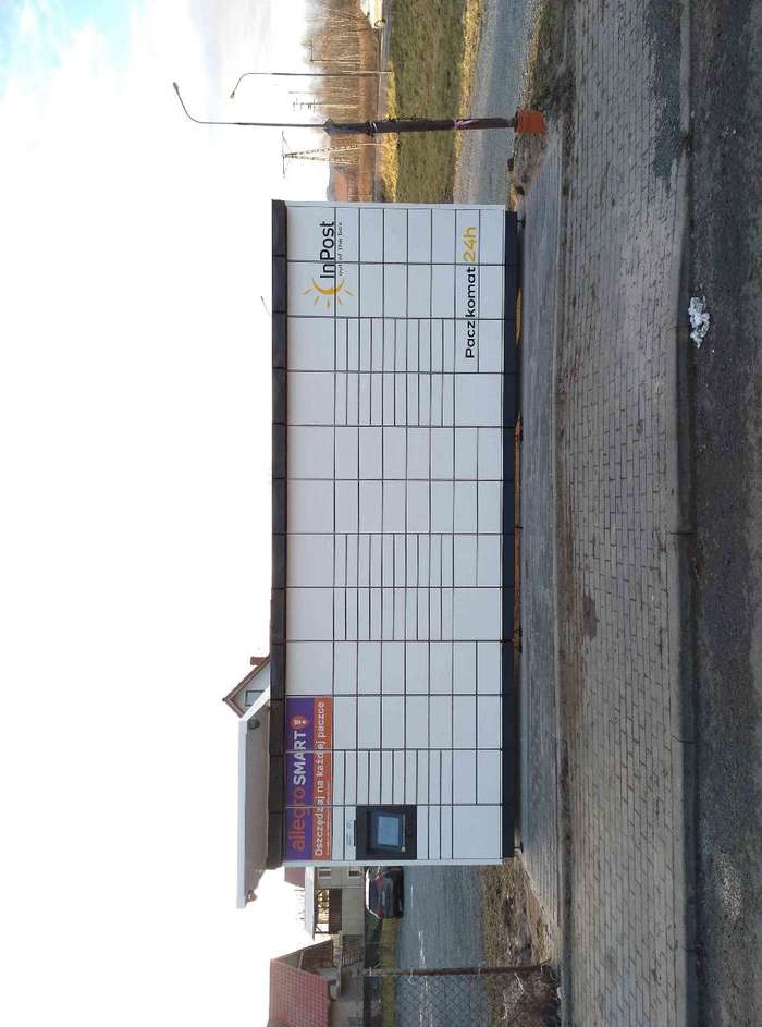 Paczkomat JGO27M Przed sklepem, obok parkingu.