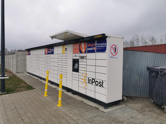 Paczkomat JLS02M Po prawej stronie stacji paliw Orlen, na końcu parkingu