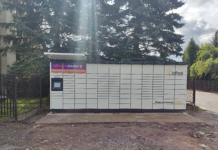 Paczkomat JSD03M Po prawej stronie od kwiaciarni, przy parkingu.