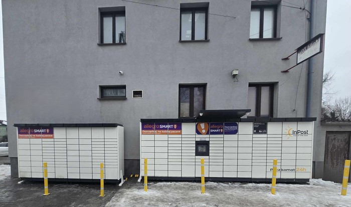 Paczkomat MLG01M Przy sklepie spożywczym, po prawej stronie budynku