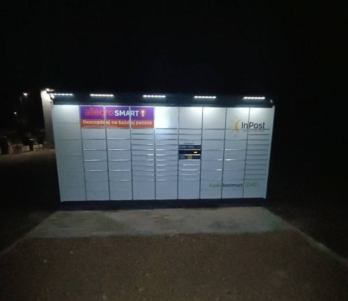 Paczkomat OLY01BAPP Przy parkingu sklepu.