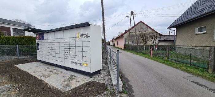 Paczkomat OPO31M Po prawej stronie budynku, przy płocie prywatnej posesji