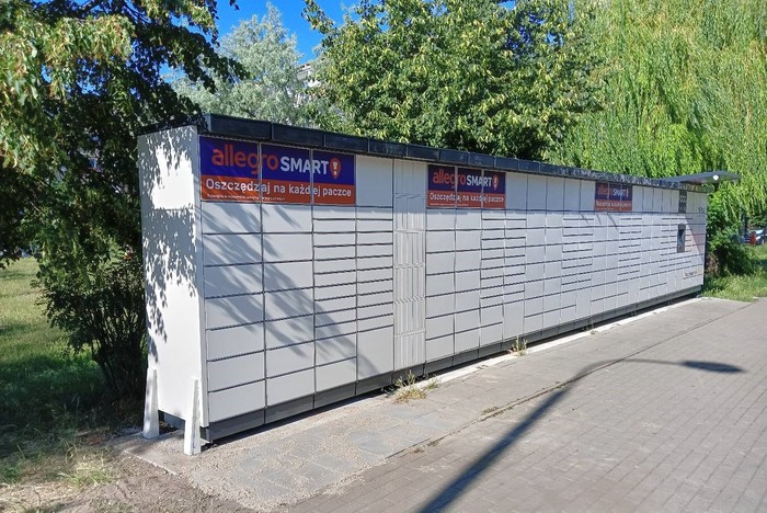 Paczkomat POZ67M Paczkomat umieszczony wzdłuż chodnika, na pasie zieleni