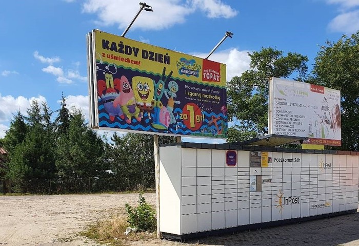 Paczkomat SIE02N Pod reklamą po lewej stronie przy parkingu