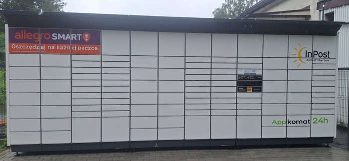 Parcel Locker SOS10BAPP od lewej strony przy furtce wejścia do budynku, pomiędzy furtką a bramą wjazdową do budynku.