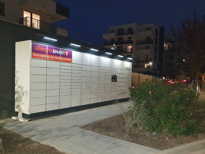 Parcel Locker WAW78BAPP parking przed wjazdem na osiedle, maszyna za szlabanem z możliwością dojścia