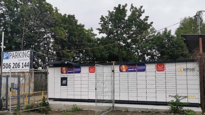 Paczkomat WRO83M W lini płotu, obok wjazdu na teren parkingu